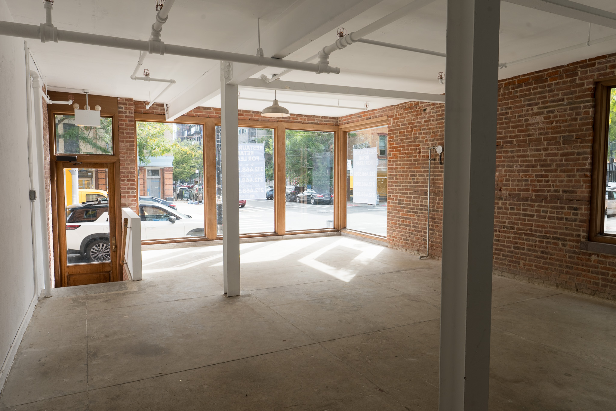 Bright vacant storefront interior with large street-facing windows and exposed brick