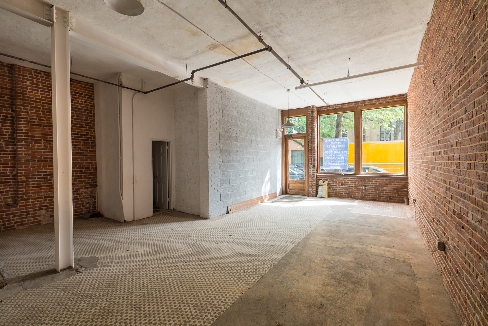 Vacant storefront interior with exposed brick walls, concrete floor, and street-facing windows