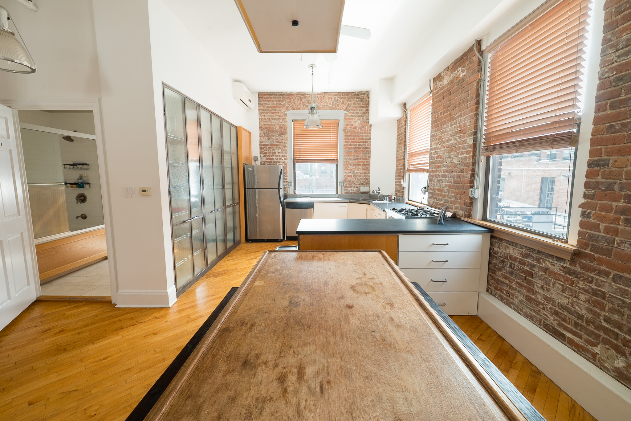 Loft kitchen and dining area with exposed brick walls, wood floors, and large windows