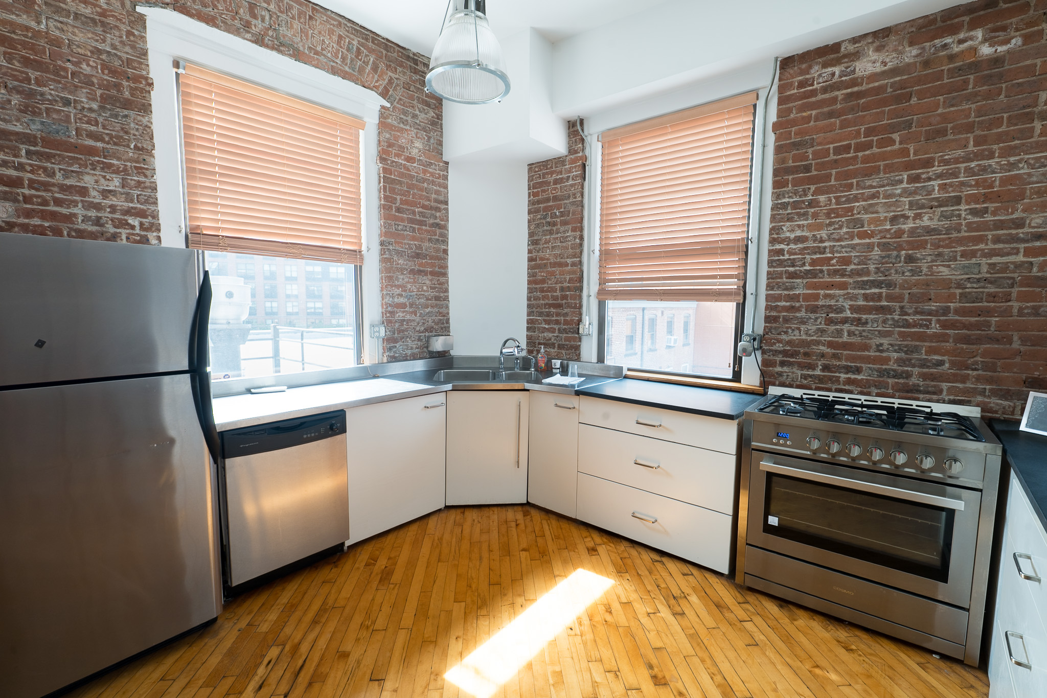 Apartment kitchen with white cabinetry, brick walls, and sunlight on wood floors