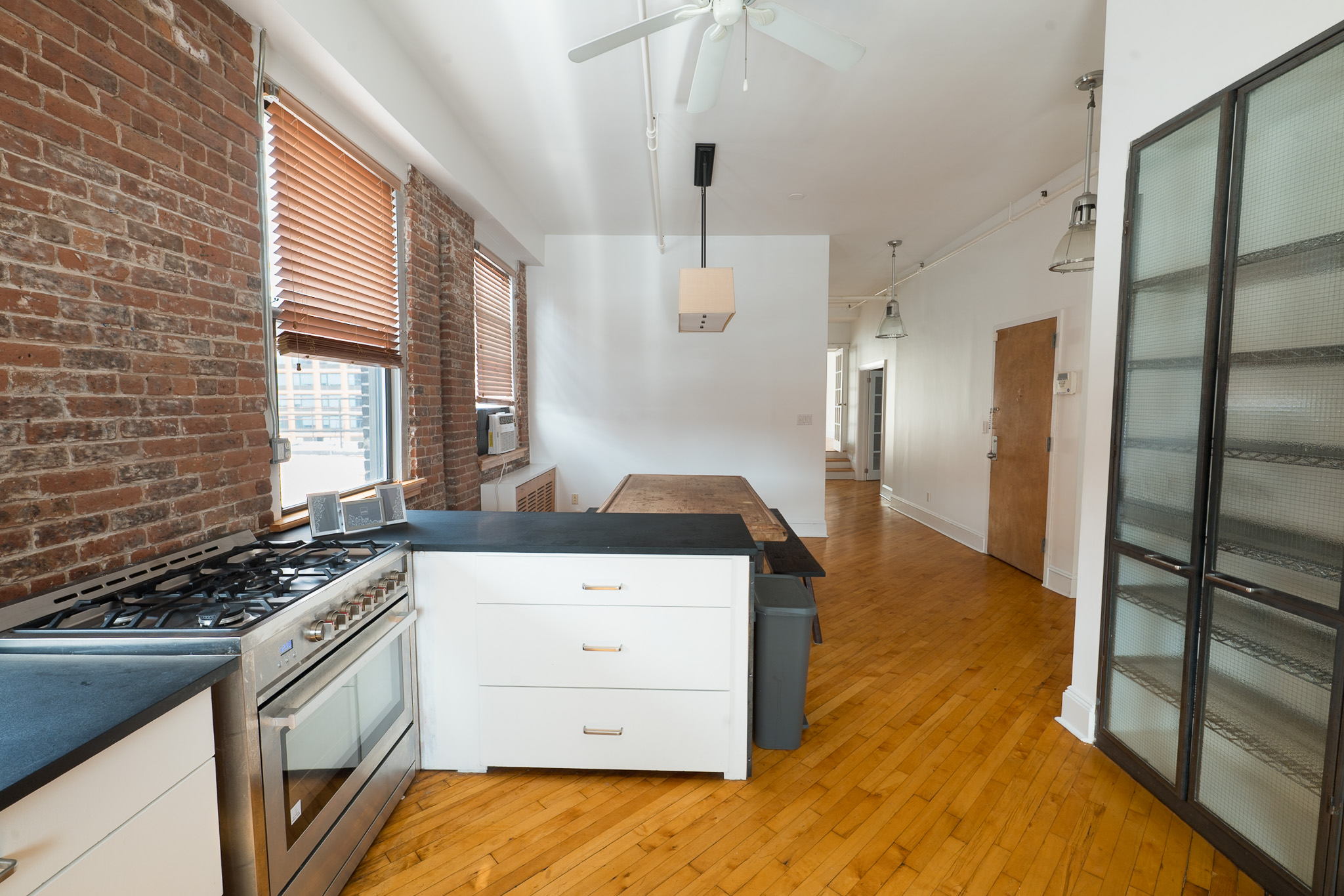 View from a loft kitchen toward the open living area with exposed brick and wood flooring