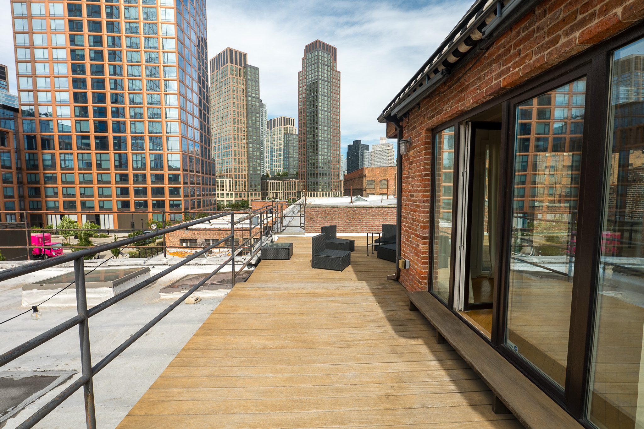 Wood-decked roof terrace beside a brick wall with city buildings in the background