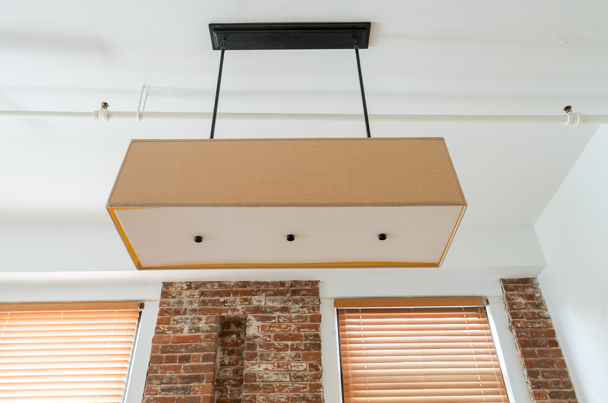 Rectangular pendant light above exposed brick and two windows with blinds