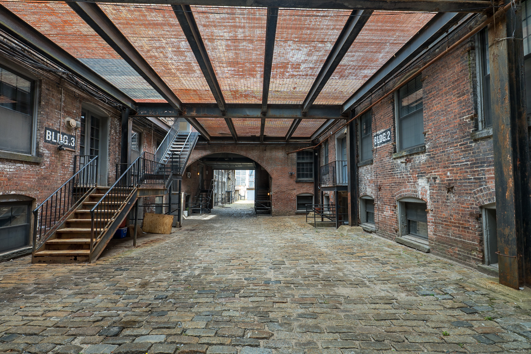 Cobblestone courtyard enclosed by brick buildings and metal stairways